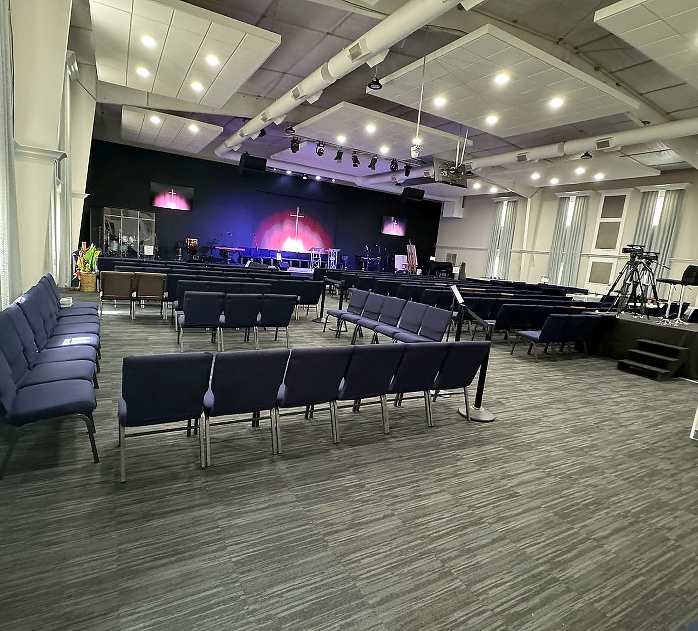 Sanctuary with blue seats, a stage and screens showing a cross